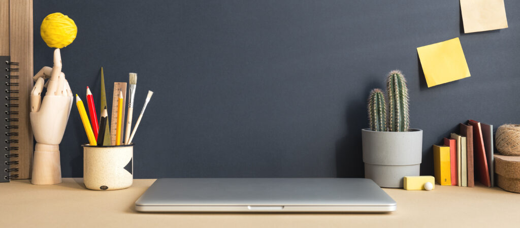 Stylish workspace and variety of school supplies, cactus and wooden hand. Creative, artistic home office. Mockup.